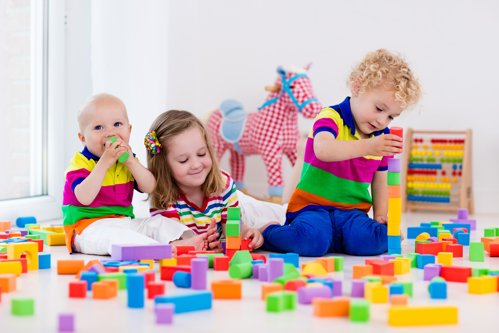 Happy preschool age children play with colorful plastic toy blocks. Creative kindergarten kids build a block tower. Educational toys for toddler or baby. Siblings having fun playing together.